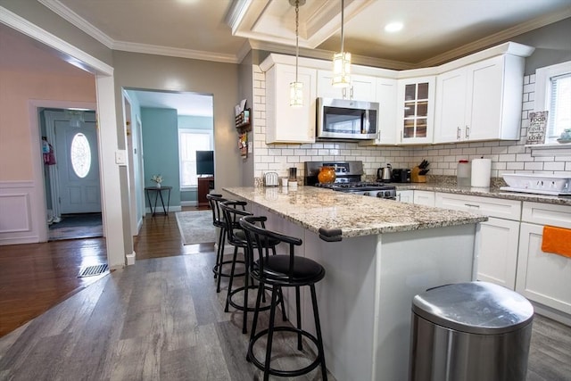 kitchen featuring decorative light fixtures, white cabinets, stainless steel appliances, and a breakfast bar area