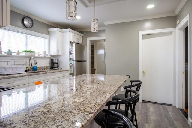 kitchen with a breakfast bar area, stainless steel refrigerator, light stone countertops, white cabinets, and sink