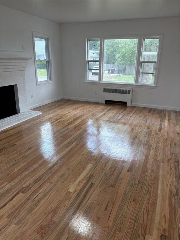 63 Bernice Ave, Brockton, MA 02301 - unfurnished living room featuring radiator heating unit, wood finished floors, and a brick fireplace