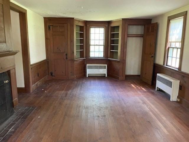 1 Pine Island Rd, Newbury, MA 01951 - unfurnished living room with radiator heating unit, a fireplace with flush hearth, wood finished floors, and plenty of natural light