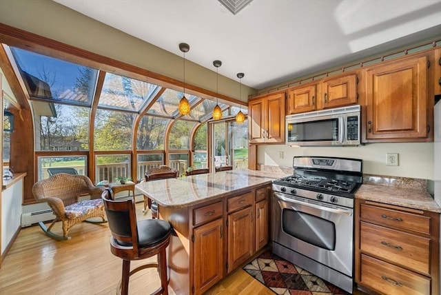 kitchen featuring brown cabinetry, decorative light fixtures, appliances with stainless steel finishes, a peninsula, and light wood-style floors