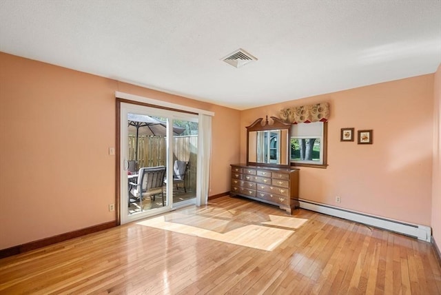 unfurnished room with baseboards, wood-type flooring, a baseboard heating unit, and visible vents