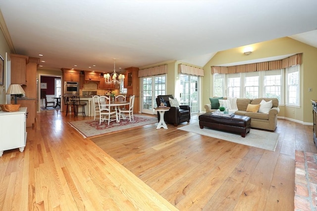 living area with an inviting chandelier, light wood-style flooring, vaulted ceiling, and a healthy amount of sunlight