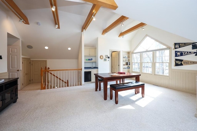 dining room with rail lighting, vaulted ceiling with beams, light colored carpet, and wainscoting