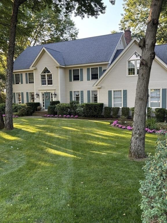 colonial home with a front lawn, roof with shingles, and a chimney