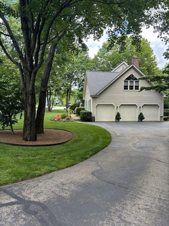 view of side of home featuring roof with shingles, an attached garage, a yard, a chimney, and aphalt driveway