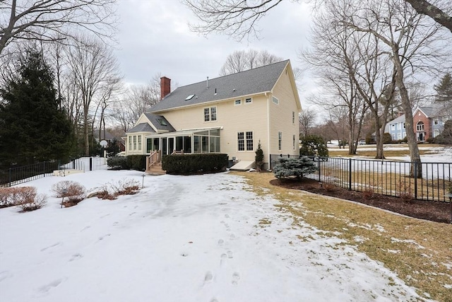 snow covered house with a chimney, a sunroom, and fence