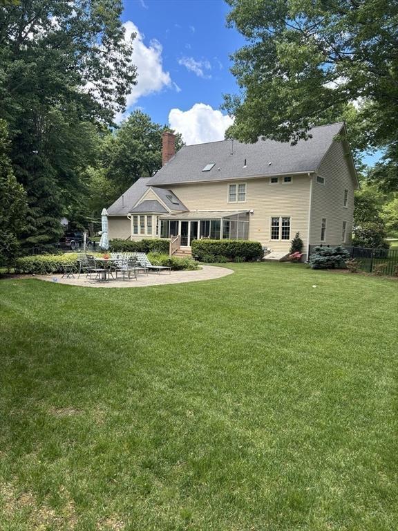 back of house featuring fence, a patio area, a lawn, and a chimney