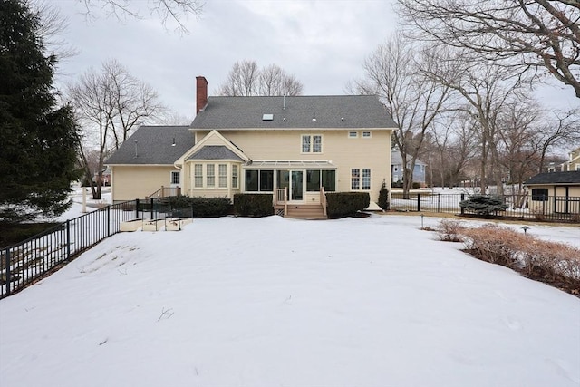 snow covered house featuring fence private yard, a chimney, and a sunroom