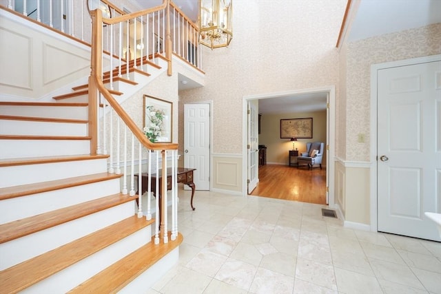 entrance foyer with visible vents, wallpapered walls, a chandelier, wainscoting, and a decorative wall