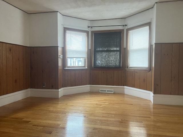 spare room with a wainscoted wall, visible vents, and wood finished floors