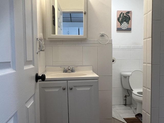 bathroom with tile walls, wainscoting, vanity, and toilet