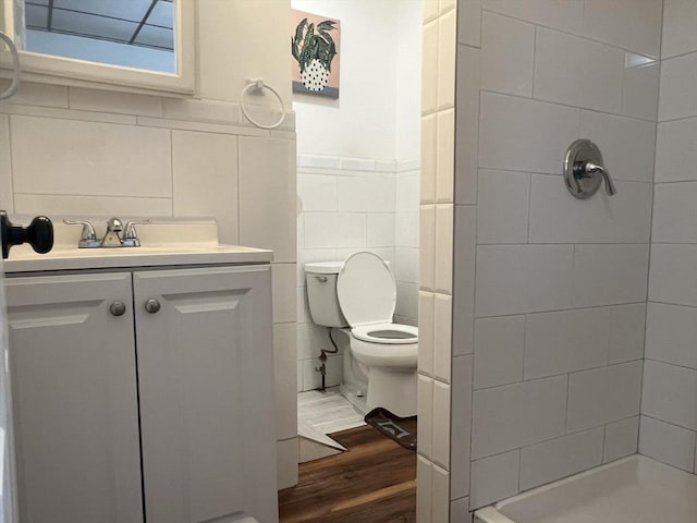 bathroom featuring toilet, wood finished floors, vanity, tile walls, and a shower stall