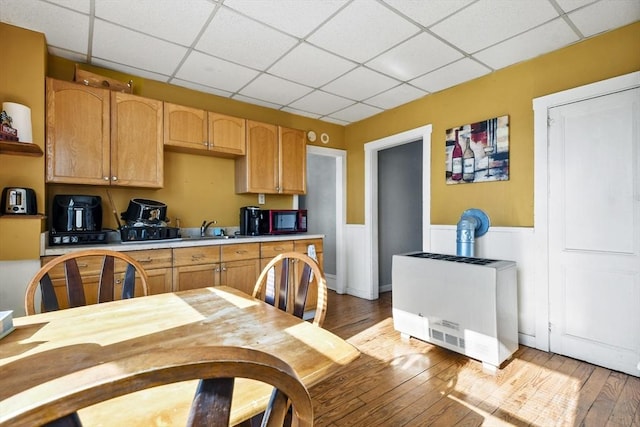 kitchen with heating unit, sink, a paneled ceiling, and light hardwood / wood-style flooring