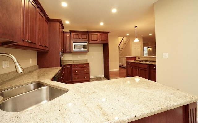 kitchen featuring light stone counters, kitchen peninsula, pendant lighting, appliances with stainless steel finishes, and sink