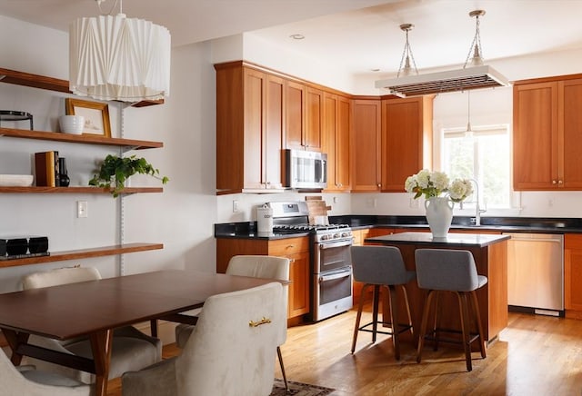 kitchen featuring a center island, hanging light fixtures, appliances with stainless steel finishes, light hardwood / wood-style floors, and a kitchen bar