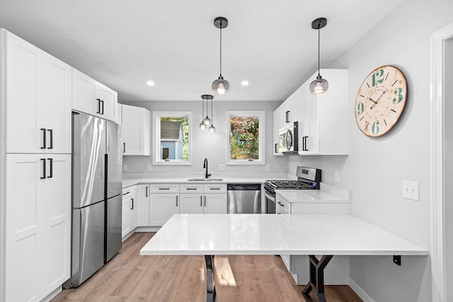 kitchen featuring appliances with stainless steel finishes, white cabinetry, sink, and hanging light fixtures