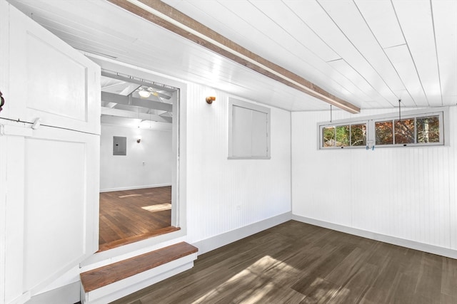 empty room with vaulted ceiling with beams, dark wood-type flooring, wooden walls, a barn door, and electric panel