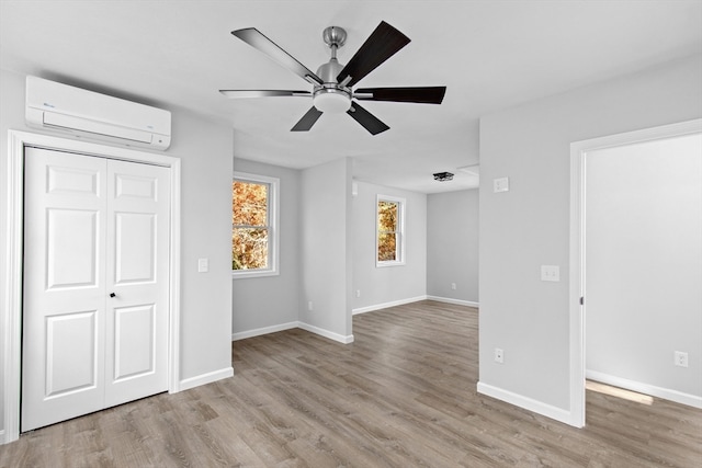 unfurnished room featuring light hardwood / wood-style floors, a wall unit AC, and ceiling fan