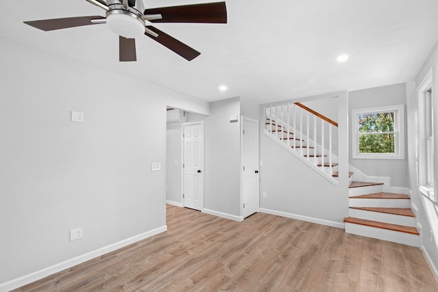 unfurnished living room with ceiling fan, a wall mounted AC, and light hardwood / wood-style flooring