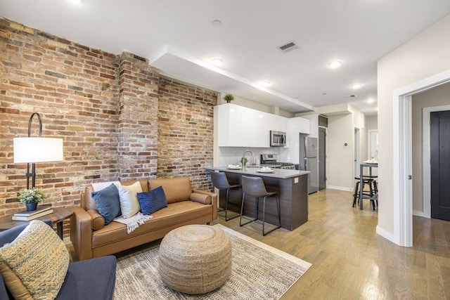 living room featuring brick wall and light hardwood / wood-style flooring