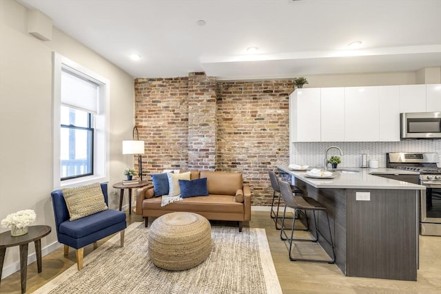 interior space with a breakfast bar, sink, appliances with stainless steel finishes, white cabinets, and backsplash