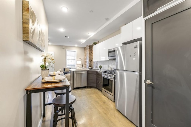 kitchen featuring white cabinetry, appliances with stainless steel finishes, light wood-type flooring, and decorative backsplash