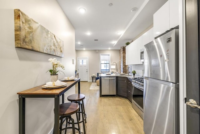 kitchen featuring a breakfast bar, tasteful backsplash, light wood-type flooring, stainless steel appliances, and white cabinets