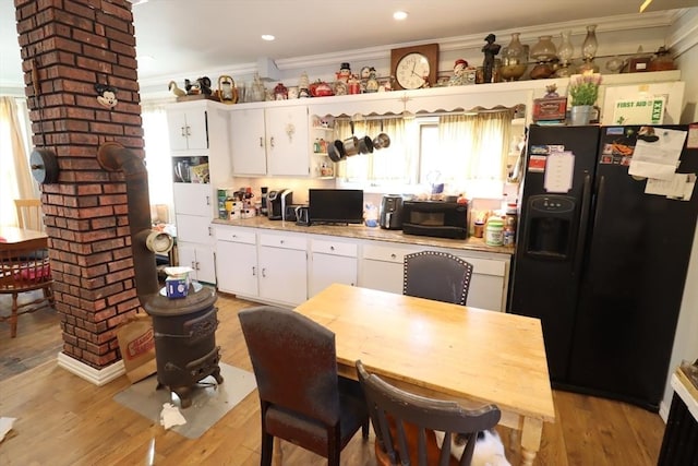 kitchen with light hardwood / wood-style flooring, ornamental molding, white cabinets, and black fridge