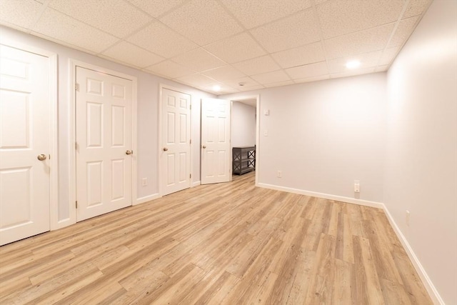 finished basement with light wood-style floors, baseboards, and a drop ceiling