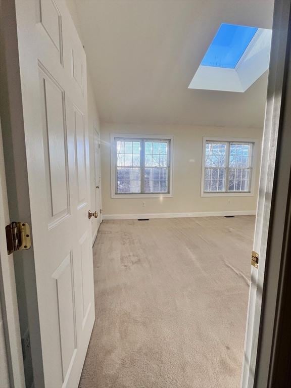 unfurnished room featuring lofted ceiling with skylight, a wealth of natural light, and light colored carpet