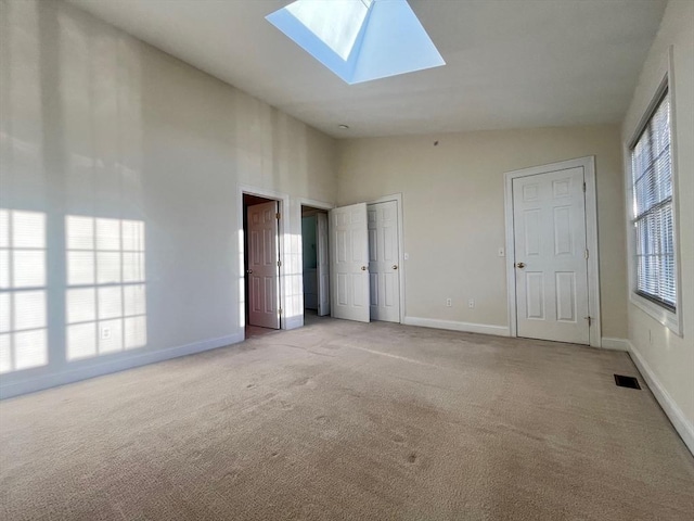 unfurnished bedroom featuring light carpet, high vaulted ceiling, and a skylight