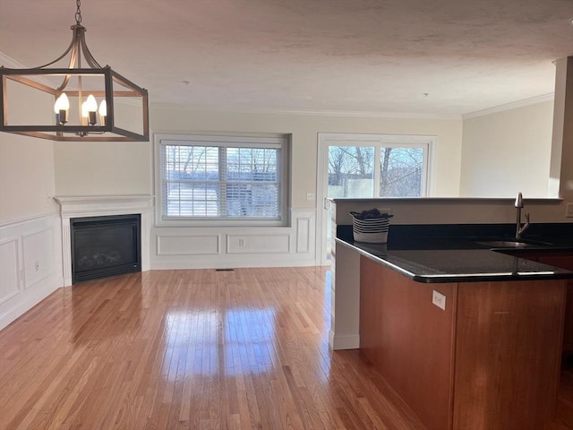 kitchen featuring sink, an inviting chandelier, crown molding, light wood-type flooring, and pendant lighting