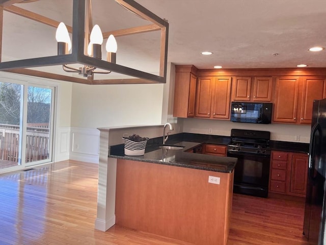 kitchen with sink, light hardwood / wood-style flooring, kitchen peninsula, dark stone counters, and black appliances