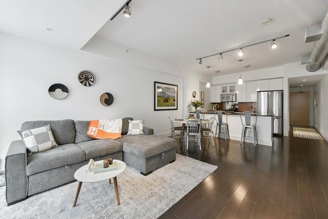 living area with track lighting, dark wood-type flooring, and baseboards