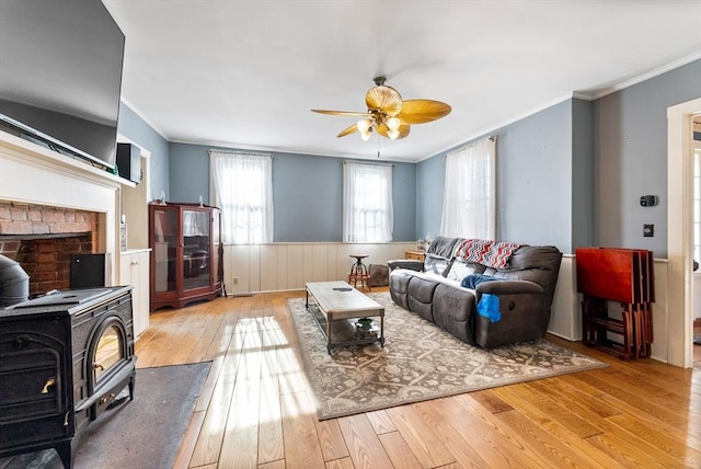 living room featuring ceiling fan, ornamental molding, light hardwood / wood-style floors, and a wood stove