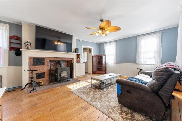 living room with ceiling fan, ornamental molding, light hardwood / wood-style flooring, and a wood stove