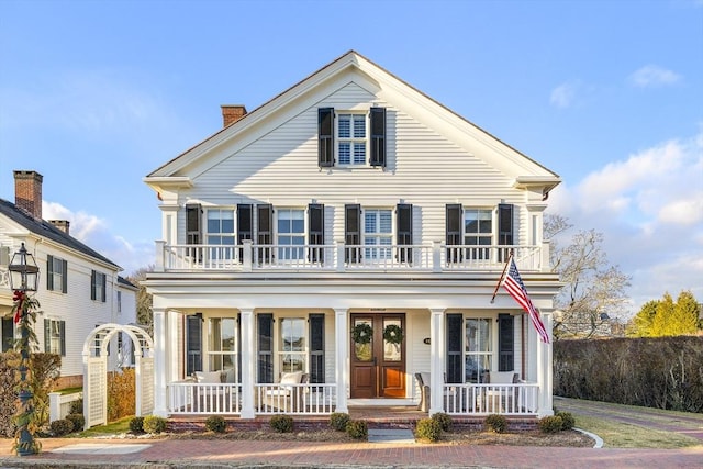 greek revival inspired property featuring covered porch, a balcony, and french doors