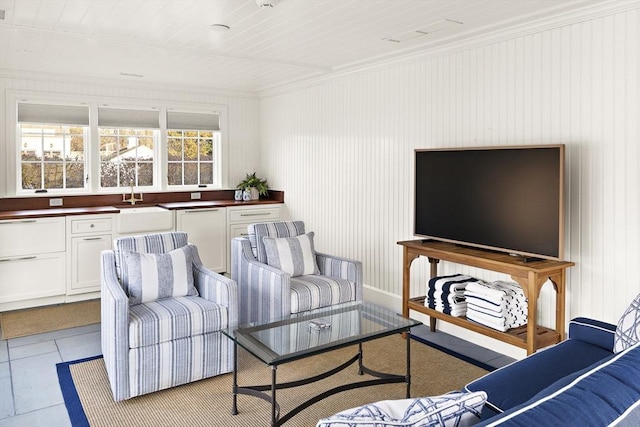 tiled living room featuring wood walls, ornamental molding, and sink