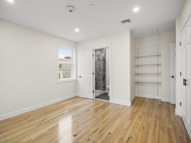 unfurnished bedroom with ensuite bathroom and light wood-type flooring