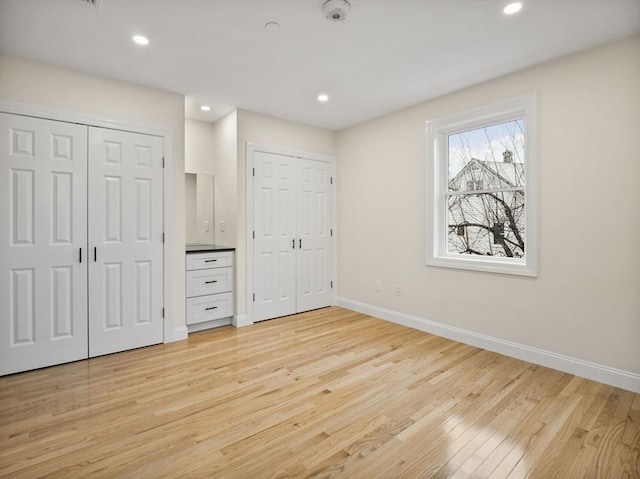 unfurnished bedroom with light hardwood / wood-style floors and two closets