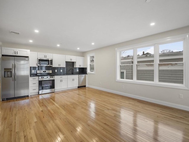 kitchen with white cabinets, appliances with stainless steel finishes, and light hardwood / wood-style flooring