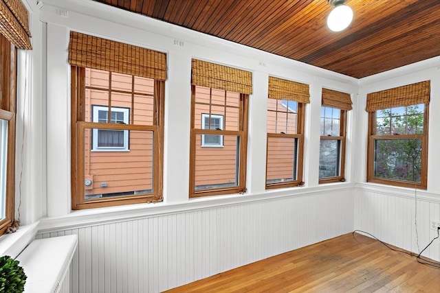 unfurnished sunroom with wood walls, wainscoting, wood finished floors, and wooden ceiling