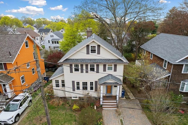 view of front of house featuring a residential view, fence, a chimney, and roof with shingles