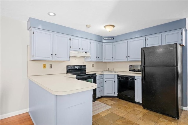 kitchen with light countertops, a sink, a peninsula, under cabinet range hood, and black appliances