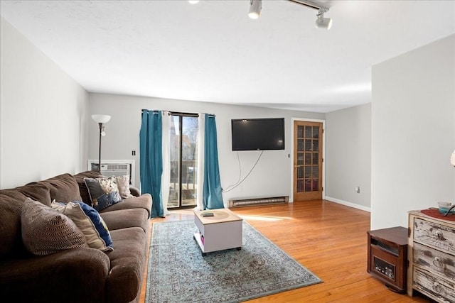 living area featuring track lighting, a wall mounted air conditioner, light wood-style flooring, and baseboards