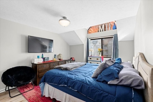 bedroom with lofted ceiling, a textured ceiling, and wood finished floors