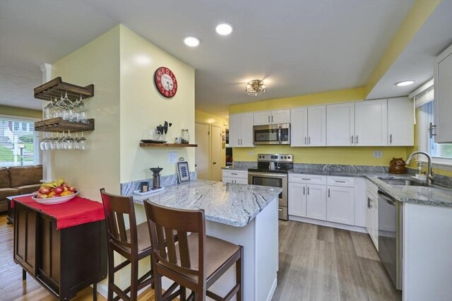 kitchen featuring stainless steel appliances, a sink, light wood-type flooring, white cabinetry, and recessed lighting