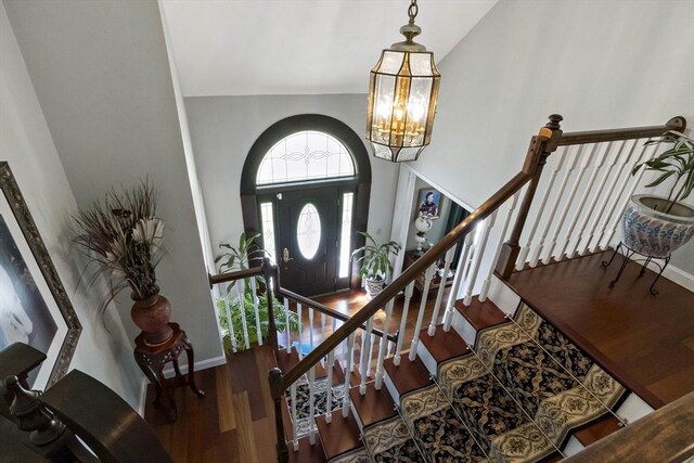 foyer entrance featuring baseboards, wood finished floors, a notable chandelier, and stairway