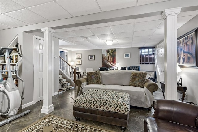 living area with baseboards, decorative columns, a drop ceiling, and stairs
